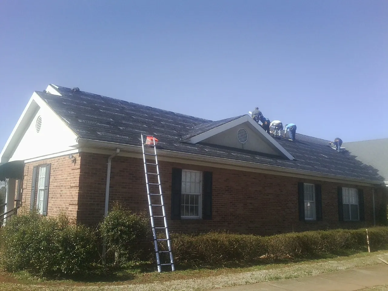 Crew tearing shingles off a brick ranch roof with a ladder set — Metal Roof Repair work by our crew in Brookhaven