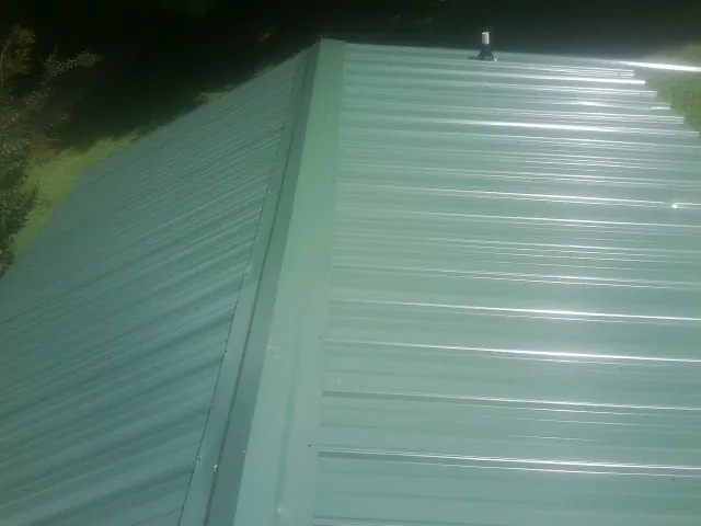 New green metal panels meeting at the ridge of a roof — Flat Roof Repair work by our crew in Brookhaven