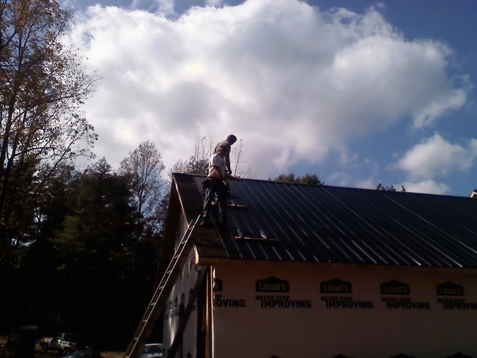 Roofer fastening dark metal panels high against a cloudy sky, from a Roof Inspection job in Brookhaven